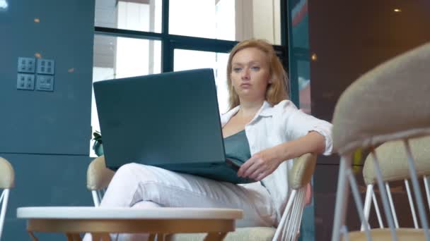 Jeune femme souriante. utilise un ordinateur portable assis dans une bibliothèque moderne . — Video