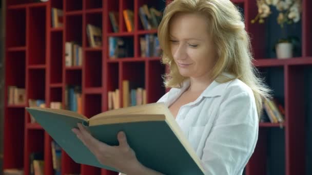 Jovem mulher lendo um livro na biblioteca no fundo de estantes — Vídeo de Stock