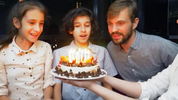 Joyeux garçon souriant soufflant des bougies sur son gâteau d'anniversaire. des enfants entourés de leur famille. gâteau d'anniversaire avec des bougies — Video