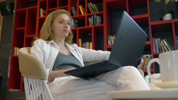 Uma jovem a sorrir. usa um laptop enquanto está sentado em uma biblioteca moderna . — Fotografia de Stock