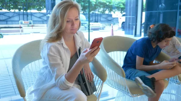 Een drukke vrouw maakt gebruik van de telefoon in de lobby van het hotel, haar kinderen naast haar zitten en ook gebruik maken van de telefoon — Stockfoto