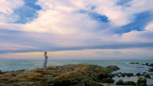 Jovem mulher caminhando em um rochoso e apreciando a vista do pôr do sol, salpicando ondas — Fotografia de Stock