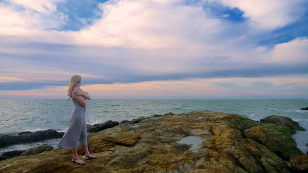 Jovem mulher caminhando em um rochoso e apreciando a vista do pôr do sol, salpicando ondas — Fotografia de Stock