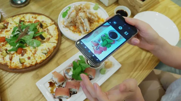 close-up. Female hands take photo of pizza on smartphone in restaurant.