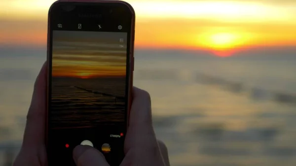 Une femme avec un téléphone portable fait une photo d'une plage tropicale au coucher du soleil . — Photo
