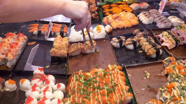 Cozinha asiática, conceito de comida. por pouco. mãos com pinças escolher sushi no mercado noturno na rua . — Fotografia de Stock