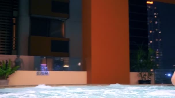 Пара расслабляется в джакузи на открытом воздухе. Счастливые молодые женщина и мужчина отдыхают в горячей воде у бассейна . — стоковое видео