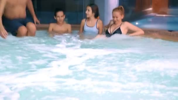 Glückliche Familie entspannen im Whirlpool im Freien. zwei Kinder Teenager, eine Frau und ein Mann entspannen in heißem Wasser in der Nähe des Pools. — Stockvideo