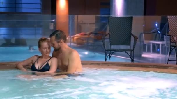 Paar entspannt in einem Whirlpool im Freien. glückliche junge Frau und Mann entspannen sich in heißem Wasser am Pool. — Stockvideo