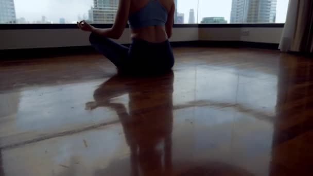 Mujer joven haciendo yoga en una habitación cerca de una gran ventana con vistas a los rascacielos . — Vídeo de stock