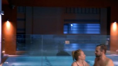 Çift açık bir jakuzide rahatlatır. Mutlu genç kadın ve adam sıcak su havuz kenarında rahatlatıcı.