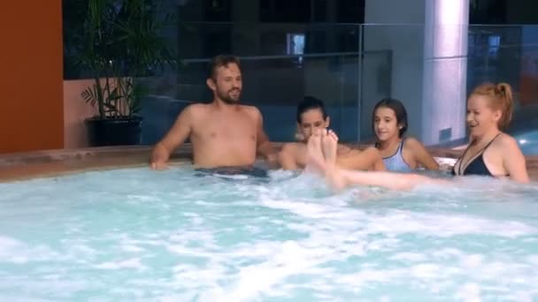 Família feliz relaxante em jacuzzi ao ar livre. duas crianças adolescentes, uma mulher e um homem relaxando em água quente perto da piscina . — Vídeo de Stock