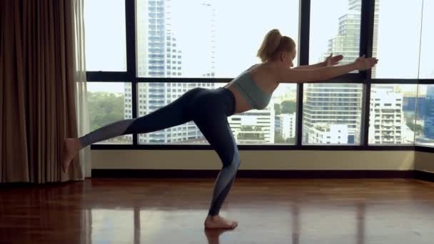 Junge Frau beim Yoga in einem Raum neben einem großen Fenster mit Blick auf die Wolkenkratzer. — Stockvideo