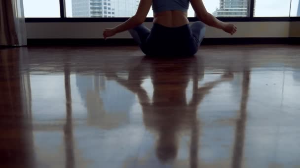 Молода жінка робить йогу в кімнаті біля великого вікна з видом на хмарочоси . — стокове відео