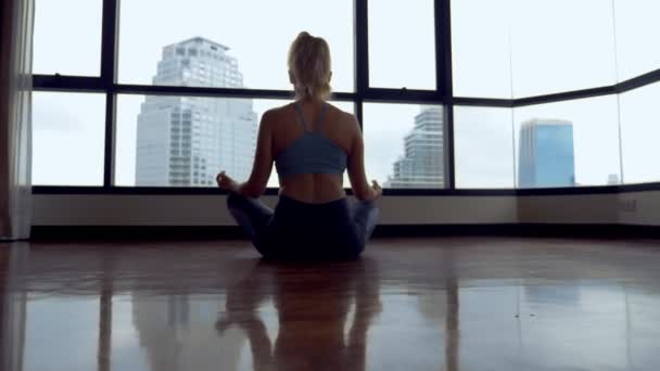 Jeune femme faisant du yoga dans une chambre près d'une grande fenêtre donnant sur les gratte-ciel . — Video