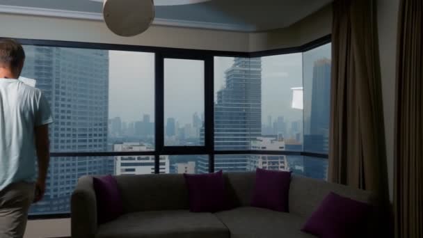 Мужчина с чемоданом на фоне небоскребов в панорамном окне — стоковое видео