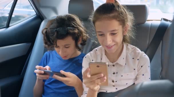 Tvillingar bror och syster använda telefonen medan man reser i bilen — Stockvideo