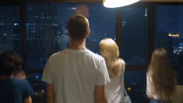 Boldog család, nő, ember és két gyermeke egy bőröndöt, a háttérben a felhőkarcolók este panoráma ablak — Stock videók