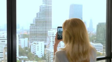 Zarif sarışın kadın telefonda bir fotoğraf yapmak. gökdelen penceresinden görünümü kadın fotoğrafları