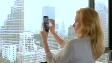 Zarif sarışın kadın telefonda bir fotoğraf yapmak. gökdelen penceresinden görünümü kadın fotoğrafları
