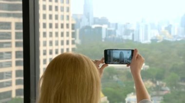 Zarif sarışın kadın telefonda bir fotoğraf yapmak. gökdelen penceresinden görünümü kadın fotoğrafları