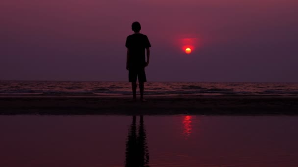 실루엣입니다. 외로운 아시아 젊은이 일몰에 버려진된 해변을 따라 평화롭게 산책. 바다 경치 — 비디오