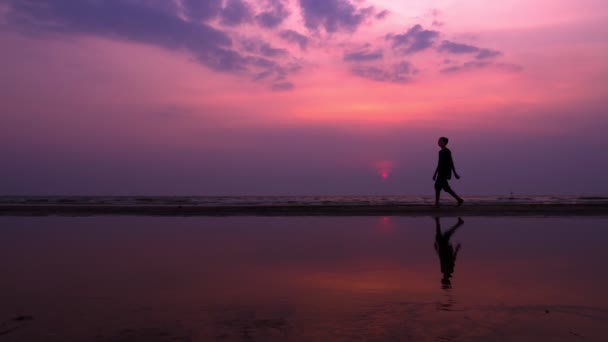 Silhueta. solitário asiático jovem caminhando pacificamente ao longo de uma praia deserta ao pôr do sol. paisagens marinhas — Vídeo de Stock