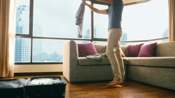 Homem bonito embala uma mala em um quarto com uma janela panorâmica com vista para os arranha-céus — Vídeo de Stock