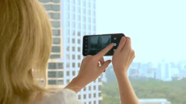 Zarif sarışın kadın telefonda bir fotoğraf yapmak. gökdelen penceresinden görünümü kadın fotoğrafları