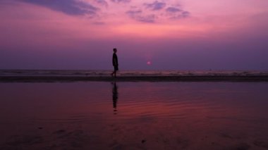 siluet. huzur içinde günbatımında ıssız bir kumsalda yürüyen yalnız Asya genç adam. deniz manzarası