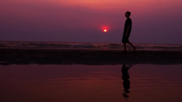 Σιλουέτα. μοναχικό Ασίας νεαρός άνδρας ειρηνικά περπατώντας μια ερημική παραλία στο ηλιοβασίλεμα. Θαλασσογραφία — Αρχείο Βίντεο