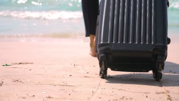 Un giovane uomo in pantaloni e una camicia classica con una valigia passeggia lungo la spiaggia sullo sfondo del mare turchese. concetto freelance, riposo — Video Stock