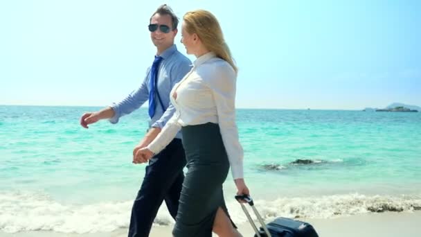 Uomo d'affari e donna d'affari con una valigia passeggiando lungo la spiaggia di sabbia bianca dell'isola — Video Stock