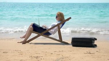 bir tembel bir beyaz kumlu plajda denizin kenarında otururken bir dizüstü bilgisayarda çalışan iş kadını. serbest veya sadakatsizlikleri kavramı.