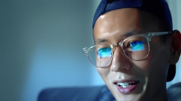 Young handsome Asian man in glasses with reflections using his laptop, sitting in the evening in the room. In the dark — Stock Video