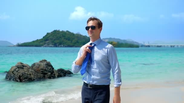 Hombre de negocios guapo en gafas de sol caminó por una playa tropical, quitándose la corbata — Vídeo de stock