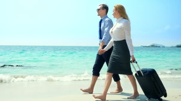Hombre de negocios y mujer de negocios con una maleta caminando por la playa de arena blanca de la isla — Vídeos de Stock