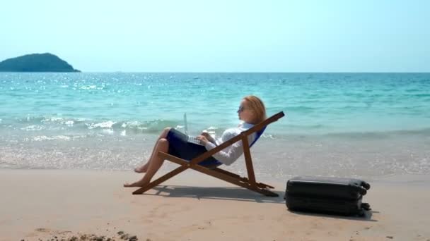 坐在海边的躺椅上, 在白色沙滩上工作的女商人。自由职业者或工作狂概念. — 图库视频影像