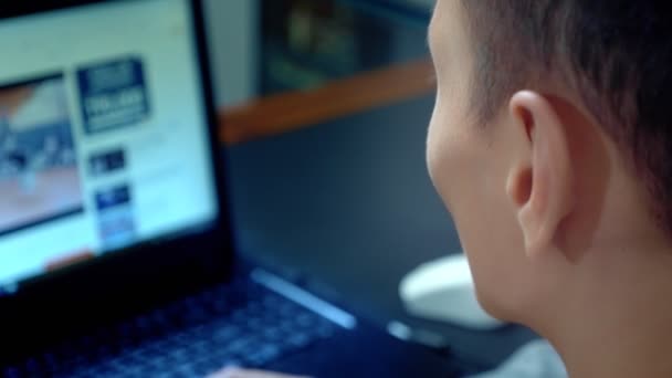 Jonge knappe Aziatische man met behulp van zijn laptop, zitten aan de balie in kantoor — Stockvideo