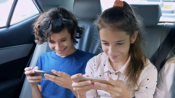 Gemelos hermano y hermana utilizar el teléfono mientras viaja en el coche — Foto de Stock