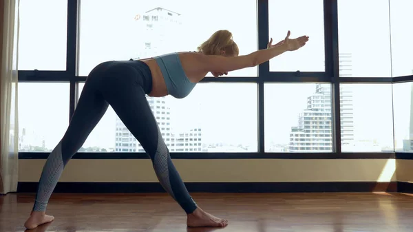 Genç kadın gökdelenler bakan büyük bir pencere yakınında bir odada yoga yaparken. — Stok fotoğraf