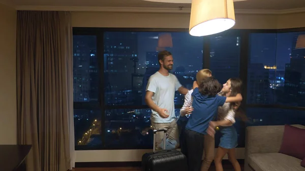 Famille heureuse, femme, homme et deux enfants avec une valise sur le fond des gratte-ciel dans la fenêtre panoramique le soir — Photo