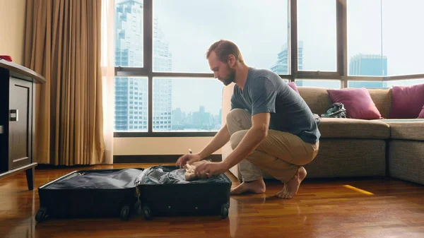 Schöner Mann packt einen Koffer in ein Zimmer mit einem Panoramafenster mit Blick auf die Wolkenkratzer — Stockfoto