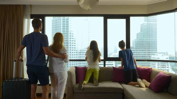 Familia feliz, mujer, hombre y dos niños con una maleta en el fondo de rascacielos en una ventana panorámica —  Fotos de Stock