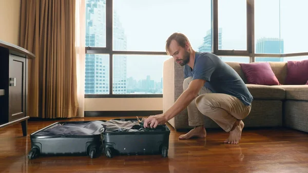 Hombre guapo empaca una maleta en una habitación con una ventana panorámica con vistas a los rascacielos — Foto de Stock