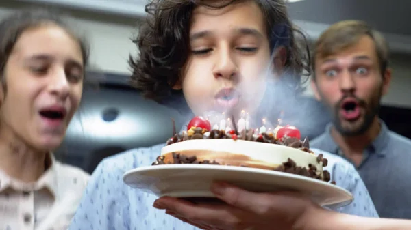 Joyeux garçon souriant soufflant des bougies sur son gâteau d'anniversaire. des enfants entourés de leur famille. gâteau d'anniversaire avec des bougies — Photo