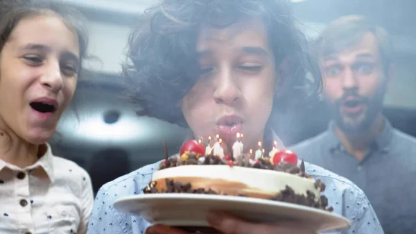 Joyeux garçon souriant soufflant des bougies sur son gâteau d'anniversaire. des enfants entourés de leur famille. gâteau d'anniversaire avec des bougies — Photo