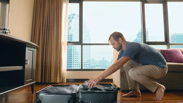 Schöner Mann packt einen Koffer in ein Zimmer mit einem Panoramafenster mit Blick auf die Wolkenkratzer — Stockfoto