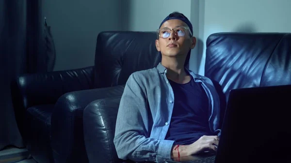 年轻英俊的亚洲男人眼镜与反射使用他的笔记本电脑, 坐在晚上的房间里。不知情 — 图库照片