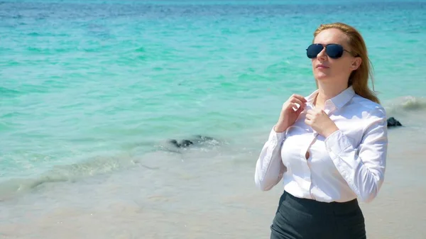 Mujer de negocios en gafas de sol en la playa. se regocija en el mar y el sol. se desabrochó la camisa y respira el aire del mar —  Fotos de Stock